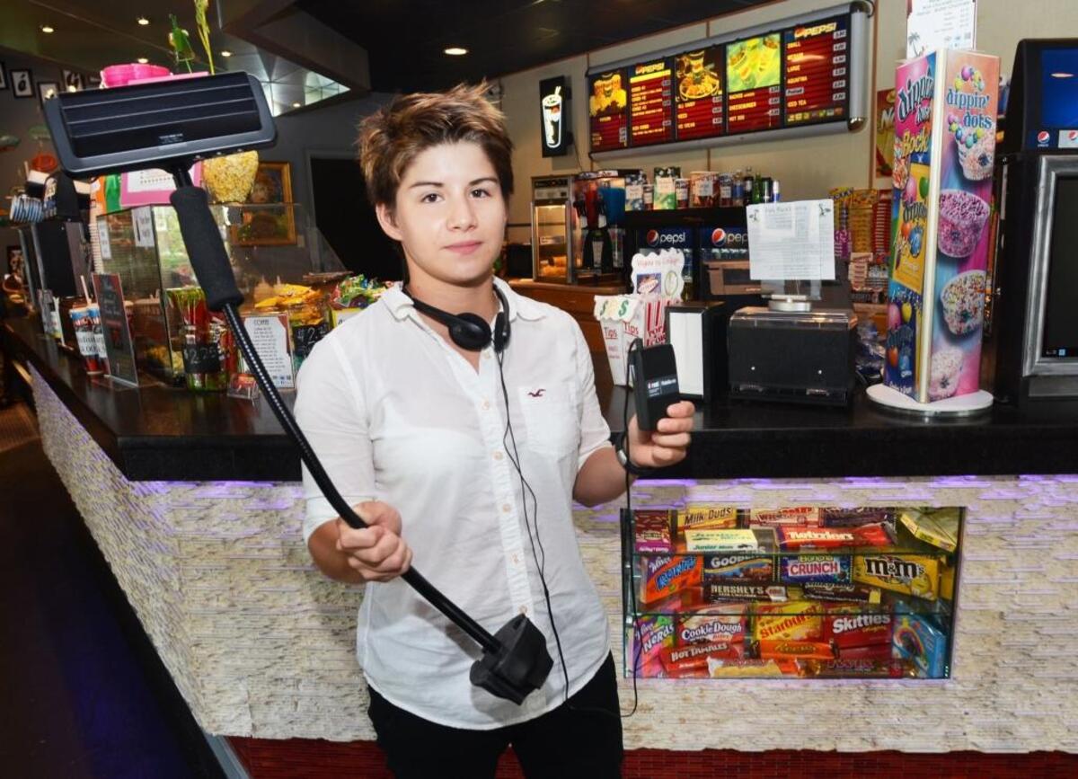 Park Plaza Cinemas employee Genesis Salcedo holds a pair of devices the movie house has installed for the benefit of its hearing impaired, visually impaired and deaf customers.