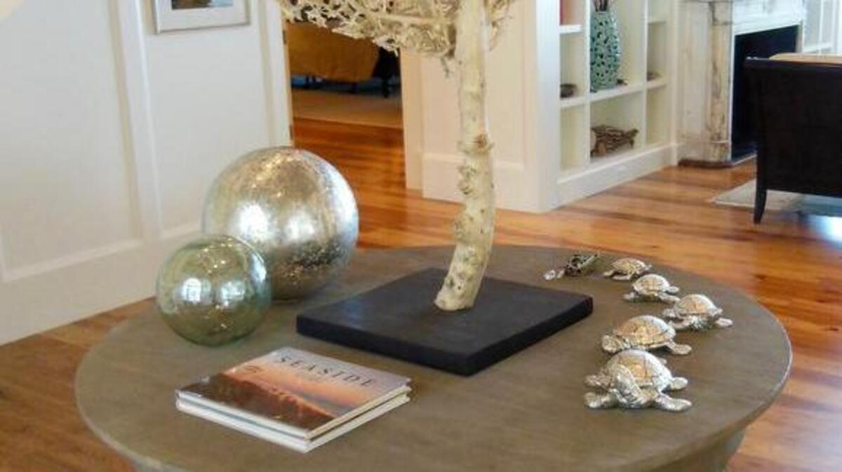 A dramatic preserved tree trunk anchors the center table in my clients’ two-story foyer. The piece was chosen for its sculptural quality, driftwood color, and coral-like appearance. The clan of marching turtle sculptures, foggy mercury glass globes, and the books on seaside architecture further evoke the coastal feel of this waterfront home. A large basket with woven twig balls continues the natural materials theme.
