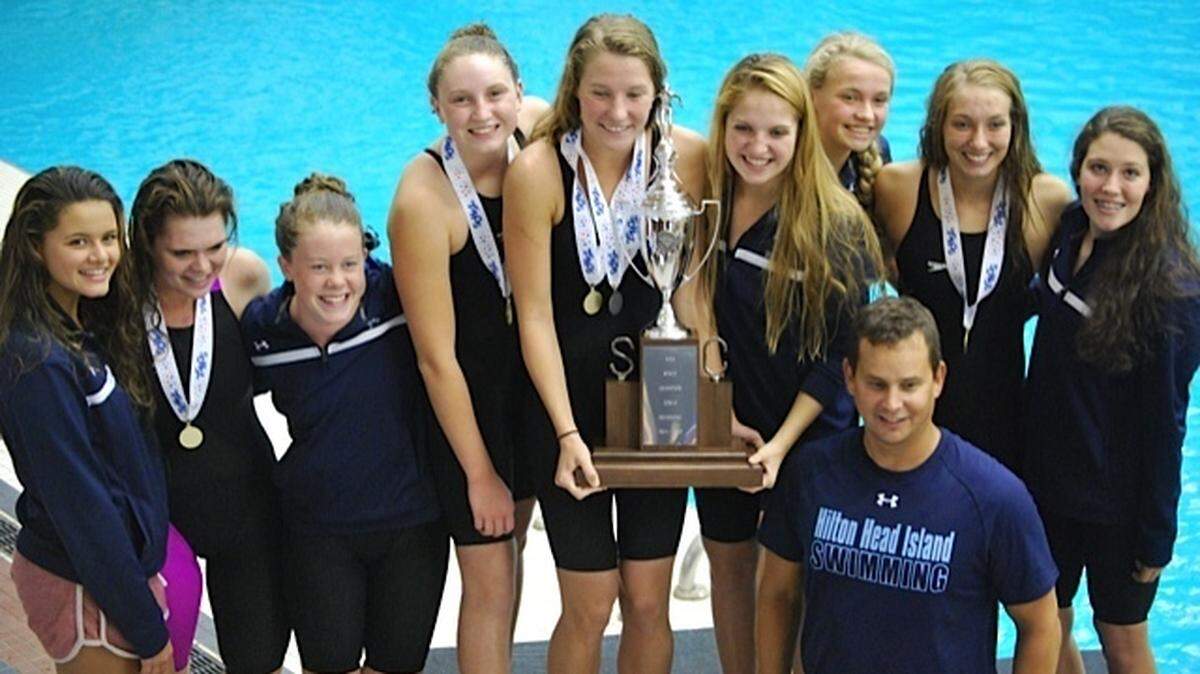 The Hilton Head Island High School girls swimming team and coach Mike Lanepose with the trophy for the 2014 Class 3-A state championship, the team's fifth straight title.