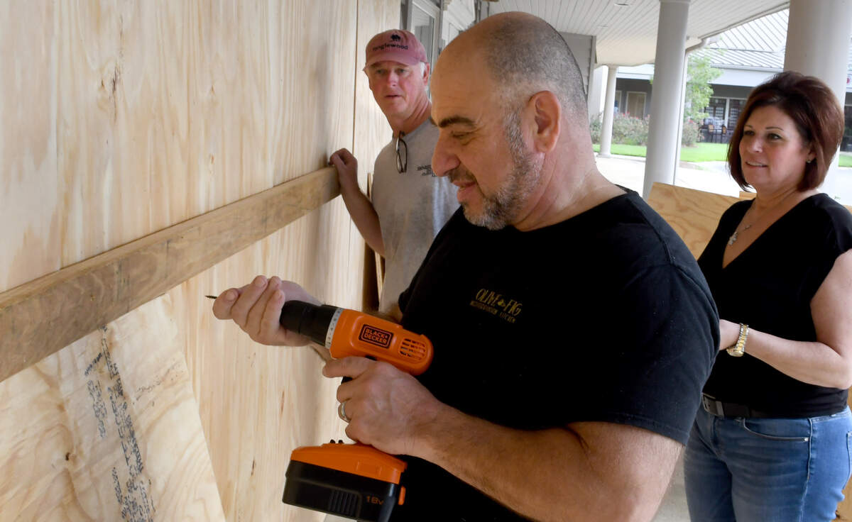 Munjid Yousif, center, and wife Tammy Yousif, right, owners of Bluffton’s Olive & Fig Mediterranean Kitchen help their neighbor Ed Wilberdin, left, board up the entrance on Labor Day to his business Signarama. Yousif said his restaurant will be open today “and as long as we can,” to help feed the people.. Wilberdin woke at 6 a.m. to buy the plywood for both businesses.