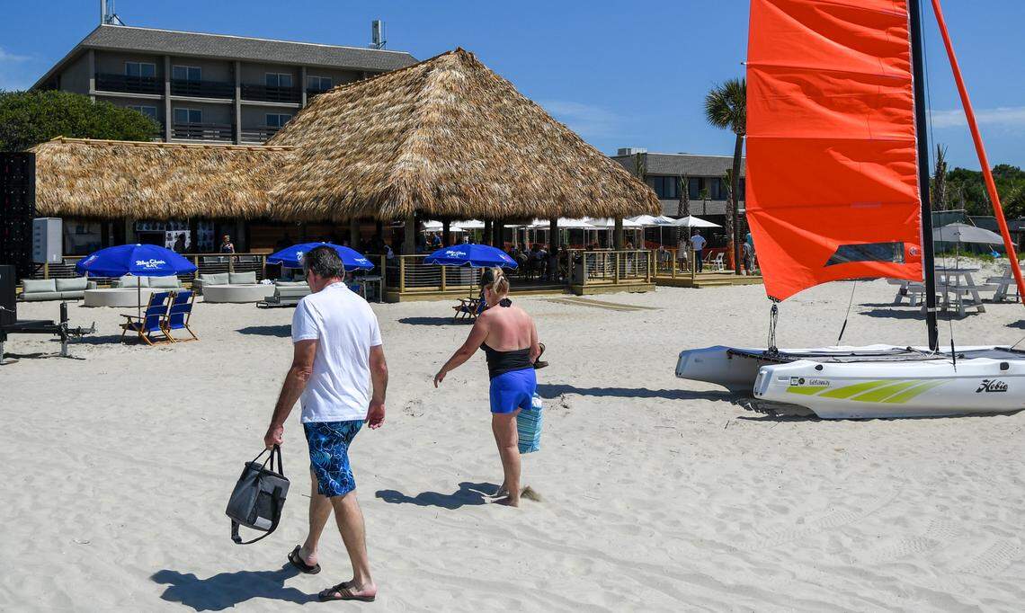 Beachgoers walk past sailing catamarans that were used for the grand opening celebration on Thursday, May 30, 2024, as the newly rebuilt and now open Tiki Hut rises in front of the Beach House Hilton Head Island.