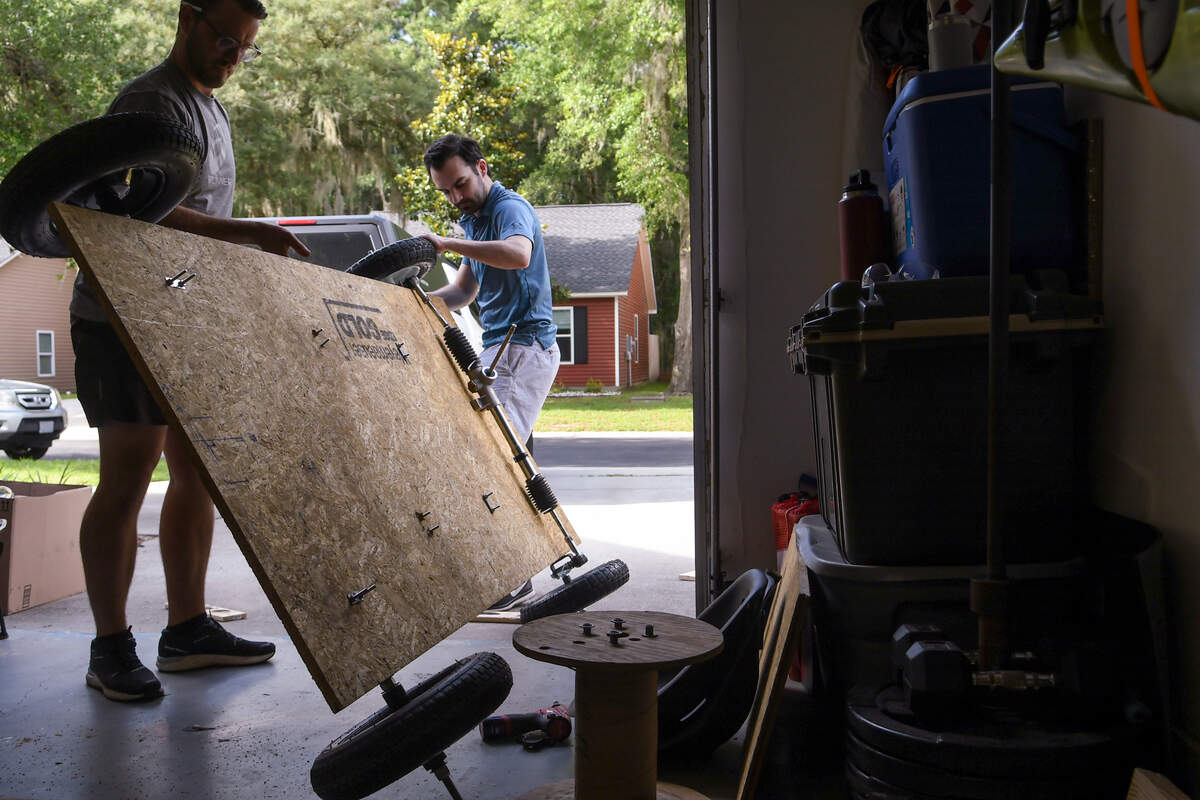 Lady’s Island resident Kody Wilson, left, and Justin Mankita lift their soapbox car on Monday, June 6, 2022 in Wilson’s garage in order to loosen the axle in order to make cuts to the pressed wood frame.