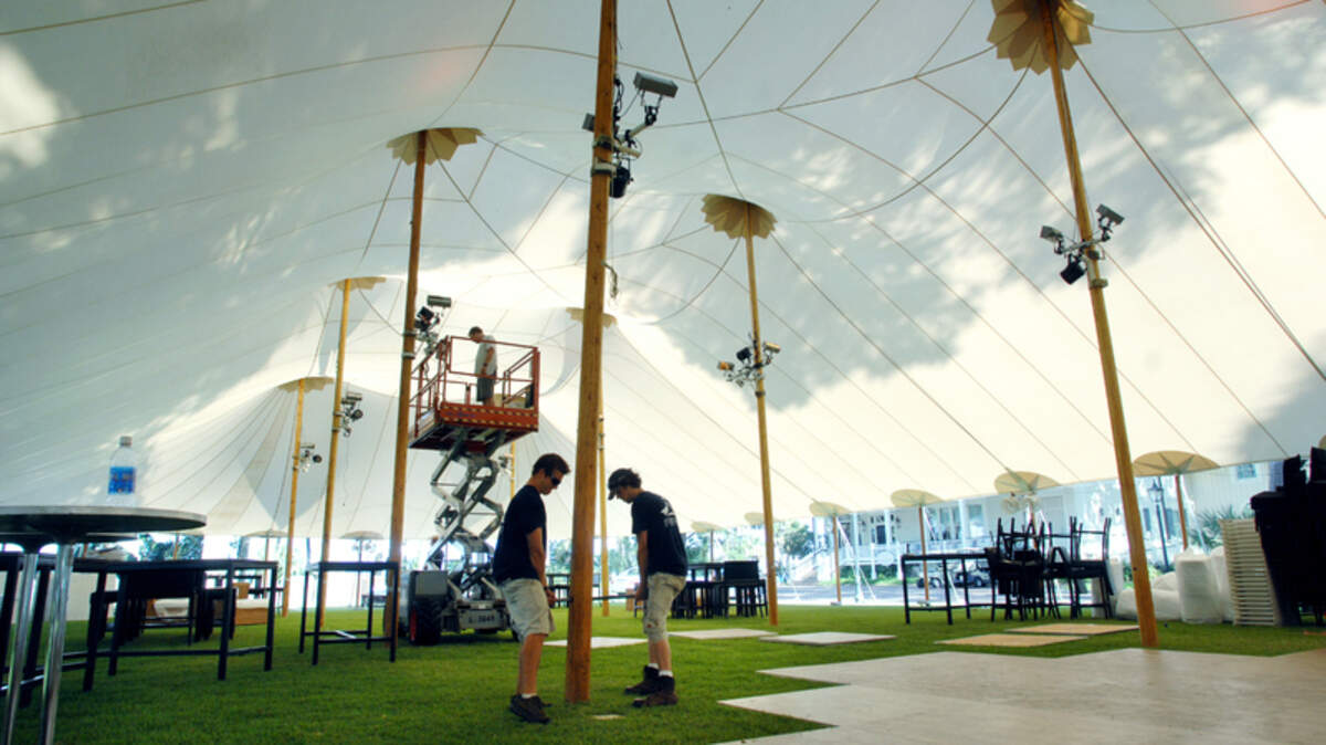 Tim Woodland, left, and Charles Goetting of Sperry Tents Southeast based in Charlottesville, Va., adjust the placement of a center pole Friday as they put up a 126-foot-long, 25-foot-high sailcloth tent at Palmetto Bluff. On the lift in the background is lighting technician Greg Eddins. The tent, on the square at Wilson Village, will be used for a lavish wedding scheduled for today.