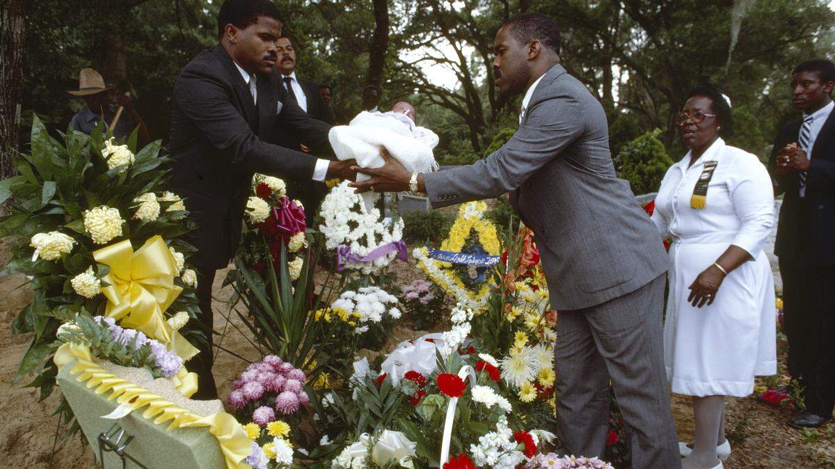 A baby is passed over her grandfather's coffin in a West African custom on St. John's Island, SC, published in a December 1987 issue of National Geographic.