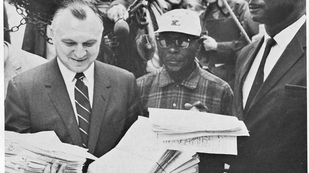 Secretary of the Interior Walter J. Hickel examines petitions protesting  a proposed chemical plant in Bluffton in April 1970. They were  delivered to Washington by the shrimp trawler Capt. Dave owned by David  Jones of Hilton Head Island, right. At center is crewman Jacob Driessen  of Hilton Head.