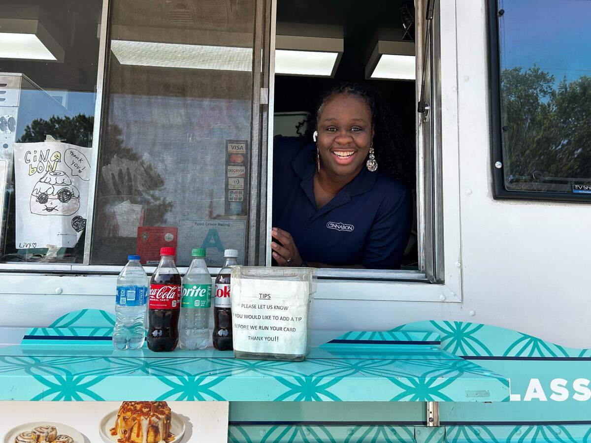 Monique Frazier smiles from the window of her Cinnabon food truck that she’s operated since 2022