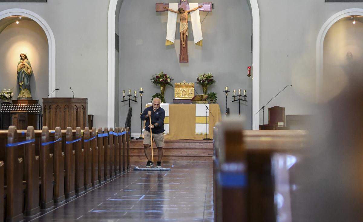 After wiping down the church pews with disinfectant, Robert Piña pushes a broom over the floor of the sanctuary on Wednesday, May 13, 2020 at St. Gregory The Great Catholic Church in Bluffton. The church reopens after the Bishop of the Roman Catholic Diocese of Charleston announced that daily Mass could resume on May 11, 2020 and the first Saturday vigil and Sunday Masses this weekend. To help keep parishioners safe, the church has incorporated social distancing, all with tape, to close every other pew, backs of pews and floors marked every six feet, and arrows on the ground directing ways to enter and leave the church. After service, the church will be closed for an hour for deep cleaning.