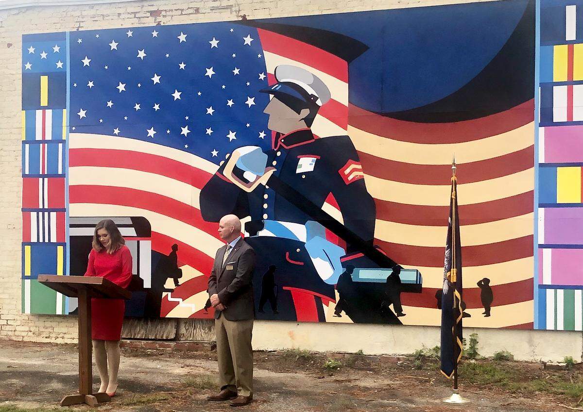 Artist Sophie Docalavich addresses the crowd at a ceremony to unveil her new mural, “Where Heroes Stood,” while Hampton County Council chairman Clay Bishop looks on Tuesday in Yemassee. The painting is dislayed across from the town’s train depot and recognizes the history of the Marine Corps’ involvement in moving recruits through the station for 50 years.