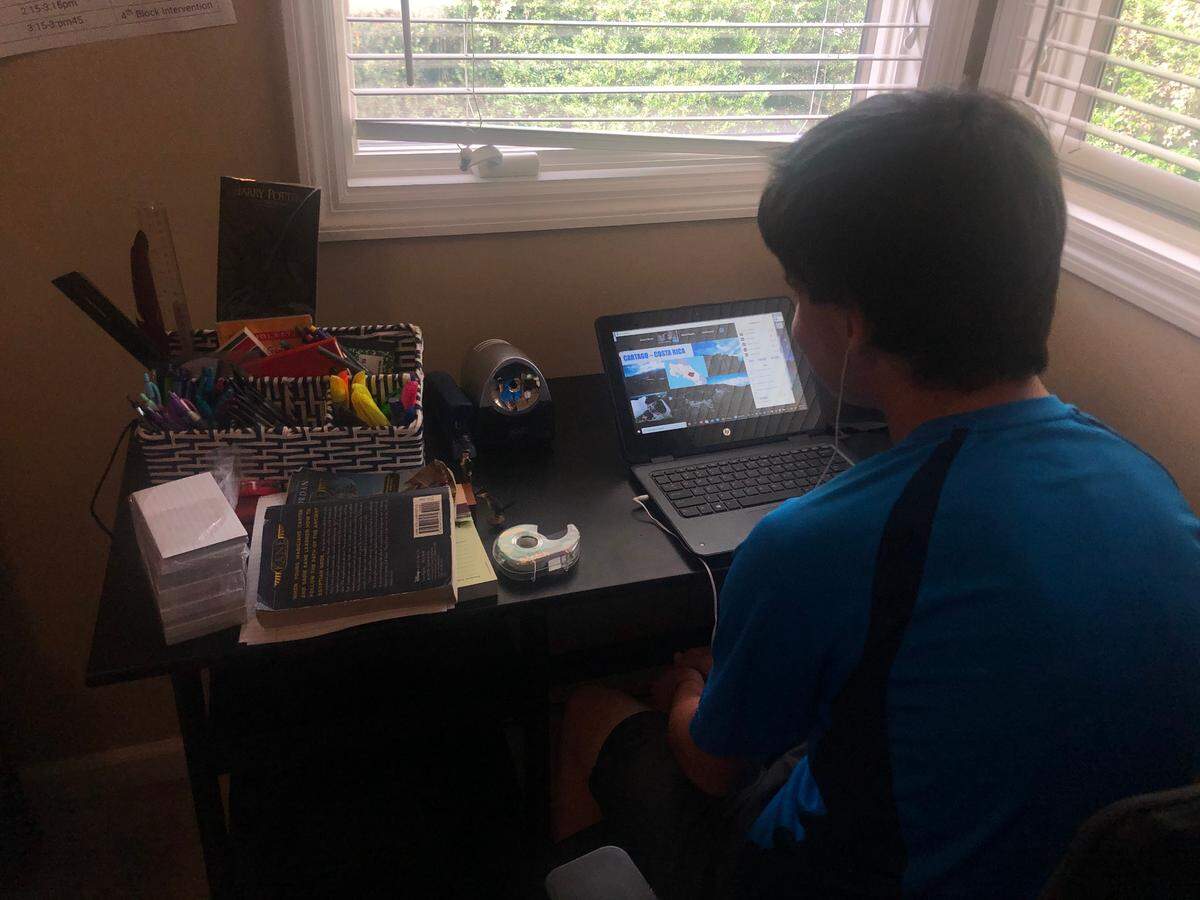 Garrett Simons sits at a desk in his bedroom to attend his first day of classes as a freshman at Hilton Head High School. He is using his school-provided laptop to attend class.