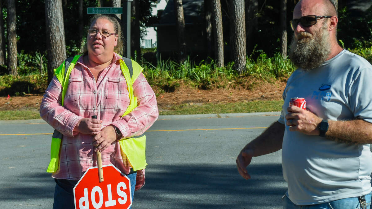 Shannon and Christopher Suits stand near the traffic circle that leads to The Reserve at Woodbridge on Thursday, Oct. 20, 2023 in Bluffton. The couple share responsibility in wearing a safety vest and holding a stop sign for their own children and those in the gated community when the children ride a Beaufort County School District bus that takes them to school.