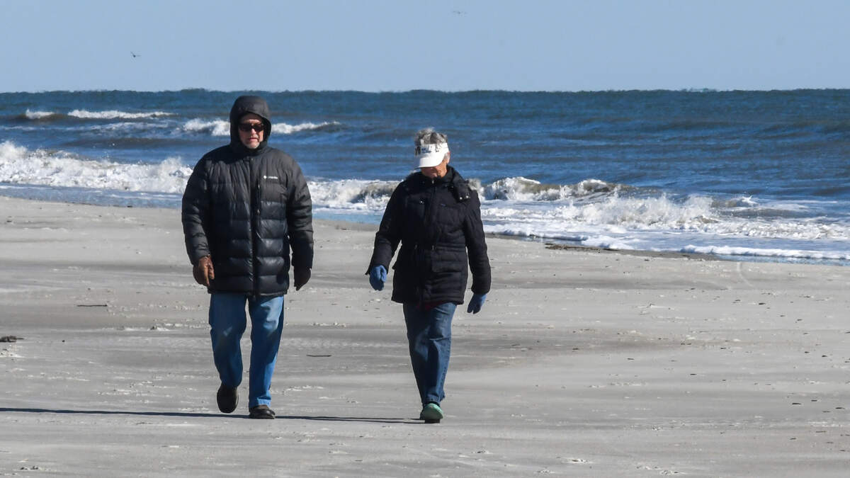 A couple wearing winter coats and gloves walks along the beach near Coligny Beach Park as a stiff breeze comes off the Atlantic Ocean on the frigid morning of Tuesday, Jan. 7, 2025, on Hilton Head Island. For the first weeks of the new year a polar vortex from the high Arctic will bring freezing temperatures to parts of the deep south.
