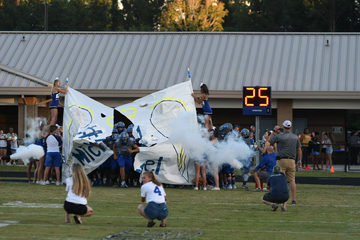 Members of the cheer squad at May River High School hold a banner honoring their fellow student Michael Mugrage, 16, with angel wings, a halo, and a number 4, who died on Aug. 28 from an aggressive form of cancer, as members of the football team crash through it to start Friday’s football game against Whale Branch Early College High School. Originally Michael, who chose the number 4, was to be an honorary captain for the team, but his deteriorating health prevented that from occurring. Instead, the football team chose to honor Michael by rotating the jersey No. 4 among players, WTOC reported.