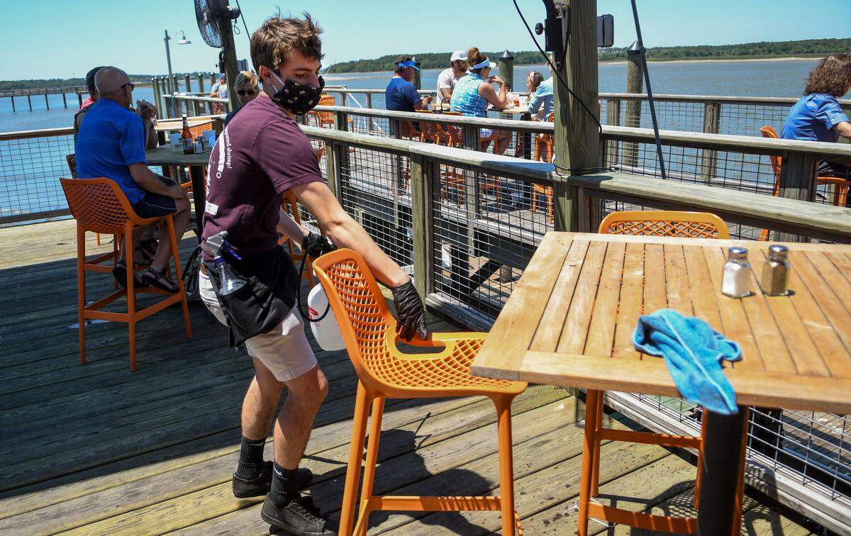 A.J. Kestler pulls a chair from the table to spray with a disinfectant on Monday, May 4, 2020 as diners enjoy their lunch at Hudson’s Seafood House on the Docks on Hilton Head Island.