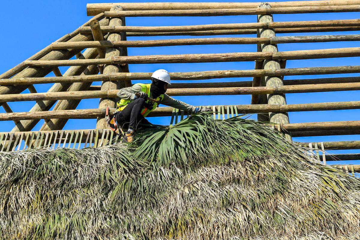 A roofer with Big Cypress Tiki Huts attaches a palm frond on Wednesday, April 24, 2024 as a new roof is built for The Beach House Hilton Head Island’s new tiki hut at Coligny Beach on Hilton Head.