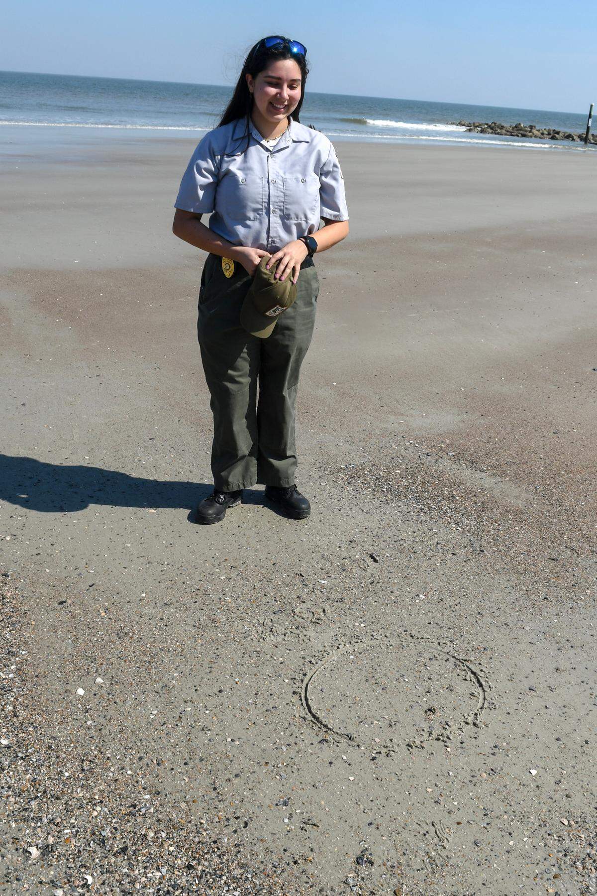 South Carolina State Park Service assistant ranger Candra Workman draws a circle around ocean sediment on Thursday, March 14, 2024 to see if newspaper reporters could find the shark tooth she had found in less than a minute at Hunting Island State Park. Workman later had to draw a smaller circle so the tooth – about the diameter of a pencil eraser – could be found.