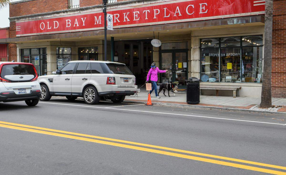 An orange traffic cone marks a free parking place along Bay Street on Monday, March 23, 2020, in front of Old Bay Marketplace as a woman walks her dogs. The City of Beaufort placed several free parking places to help restaurants with take out orders during the COVID19 virus outbreak.