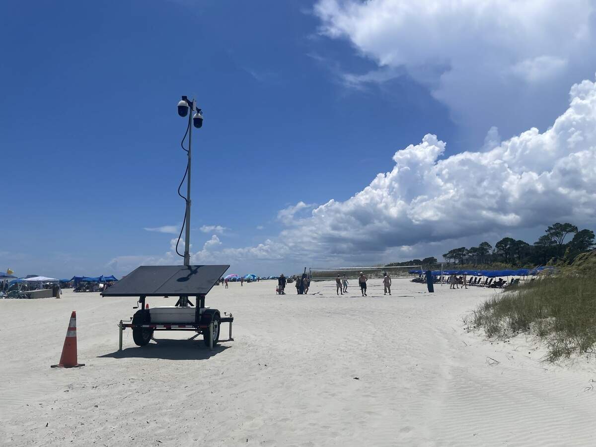 Men play volleyball on Coligny Beach near the Tiki Hut as a Beaufort County Sheriff’s Office surveillance trailer watches from above on Monday, July 6, 2026. Two days earlier, a shooting near the court injured eight people and sent crowds of beachgoers running.