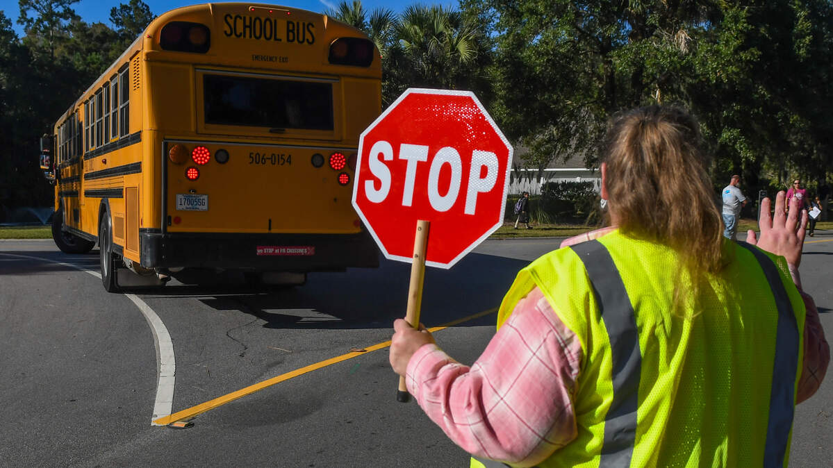 Shannon Suits holds a sign to stop vehicular traffic and waves to her children as a Beaufort County School District bus drops off elementary school-aged children at the traffic circle that leads to The Reserve at Woodbridge on Thursday, Oct. 20, 2023 in Bluffton.