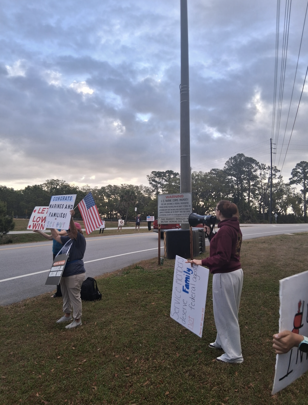 Standing beside a sign marking U.S. Marine Corps property, protesters held signs and spoke through megaphones on April 3, 2026, opposing the potential presence of federal immigration enforcement officers at Parris Island recruit graduation events.
