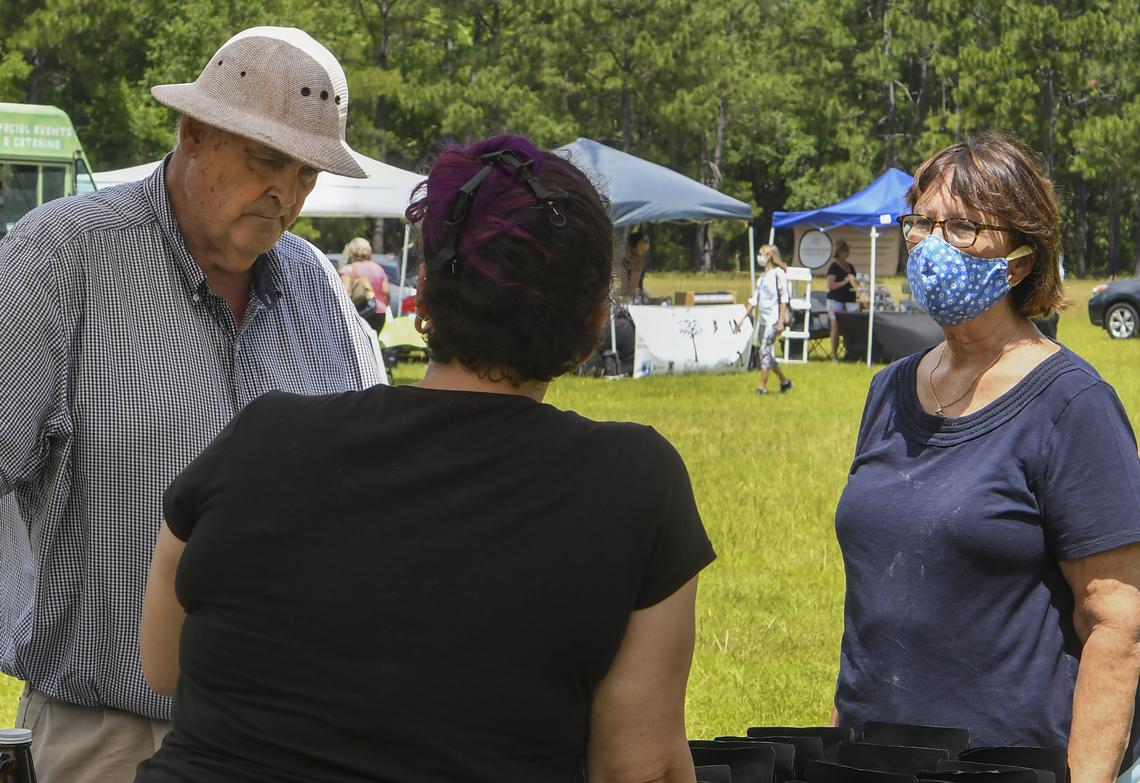 Hilton Head Island residents George Westerfield, left, and wife, Sherry Westerfield, right, speak to a sales person at a stand at the Hilton Head Farmers Market on the afternoon of Tuesday, May 19, 2020, on the grounds of the Coastal Discovery Museum. George, who had his face mask in his pocket, prefers not wearing it outdoors saying, “I wear it in all stores. It’s respectful of others.”