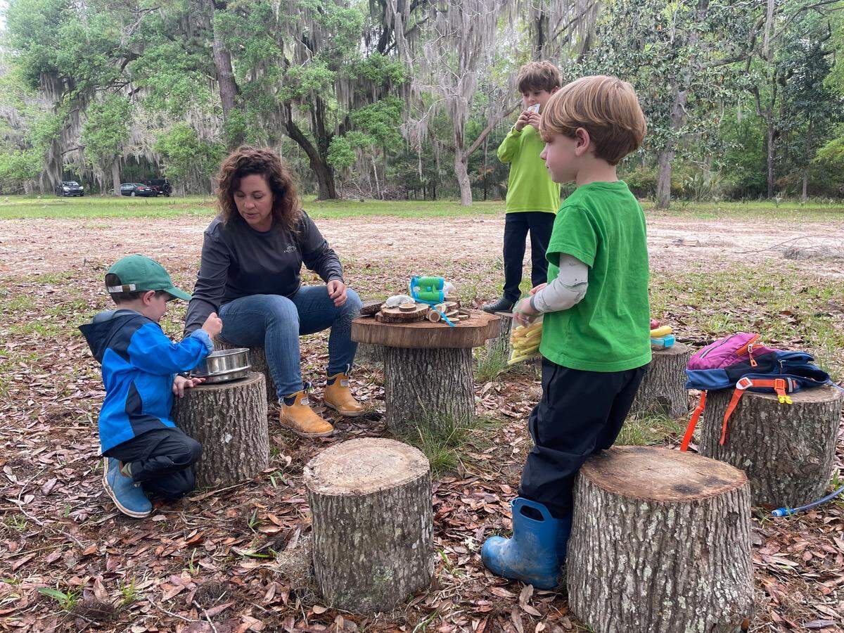 Students gather around a circle of tree stumps for snack time and reading.