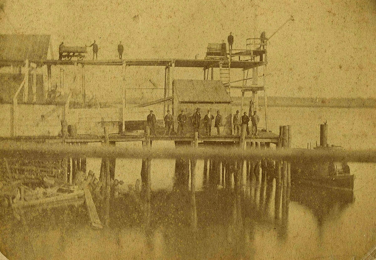 Photograph of phosphate wharf at Beaufort, S.C. with men on docks, steamer ready for loading and workers with rail cart; dated June 1874.