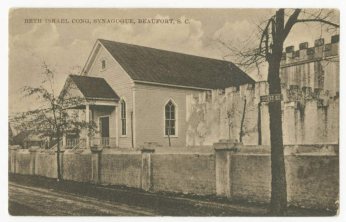 A postcard shows a photo of the early days of the Beth Israel Synagogue on Scott Street in Beaufort. The synagogue was chartered in 1905. It opened in 1908. It is located next to The Beaufort Arsenal, a historic armory built in 1798. The synagogue and armory still stand in 2025.