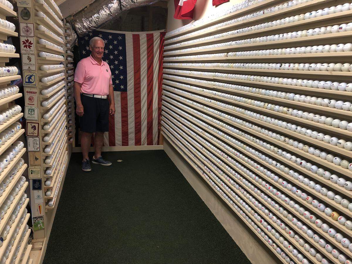 Doug Coupe stands on the putting green in the attic of his Bluffton home surrounded by a small portion of his golf ball collection.