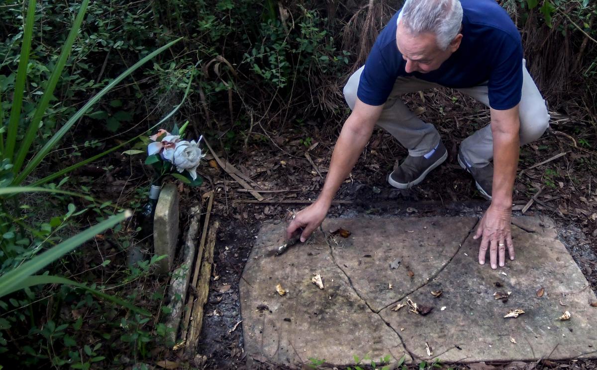 Cast in the shadow of the Cherry Hill Plantation live oak estimated to be more than 3 centuries old, Chuck Yahres clears debris from the grave marker of Mary Pope at the base of the tree on Sept. 21, 2022, in the town of Port Royal.