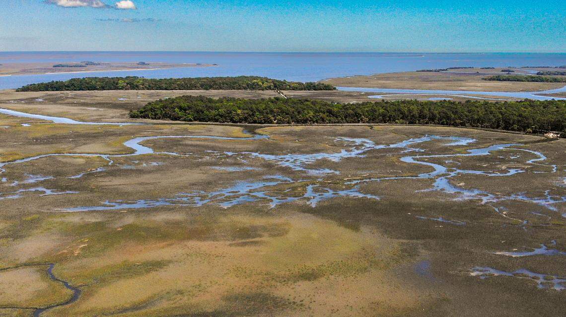 Pine Island, top, can be accessed by a private, one-lane dirt road that winds through a heavily forested peninsula of St. Helena Island as seen in this drone photo taken on April 12, 2023. A nearly half mile long causeway with a bridge, as seen between the two forested pieces of land then brings you onto Pine Island.