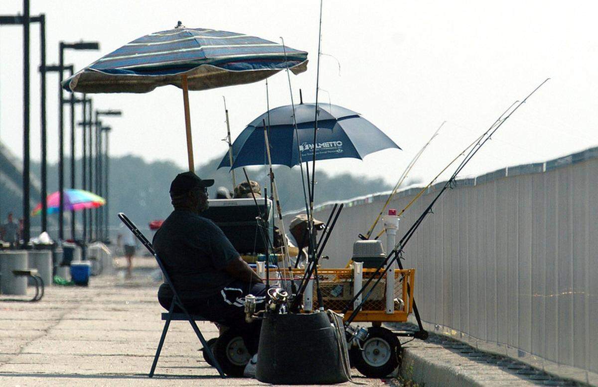 People are seen fishing and using umbrellas to provide some shade from the heat at the Broad River Bridge fishing pier.