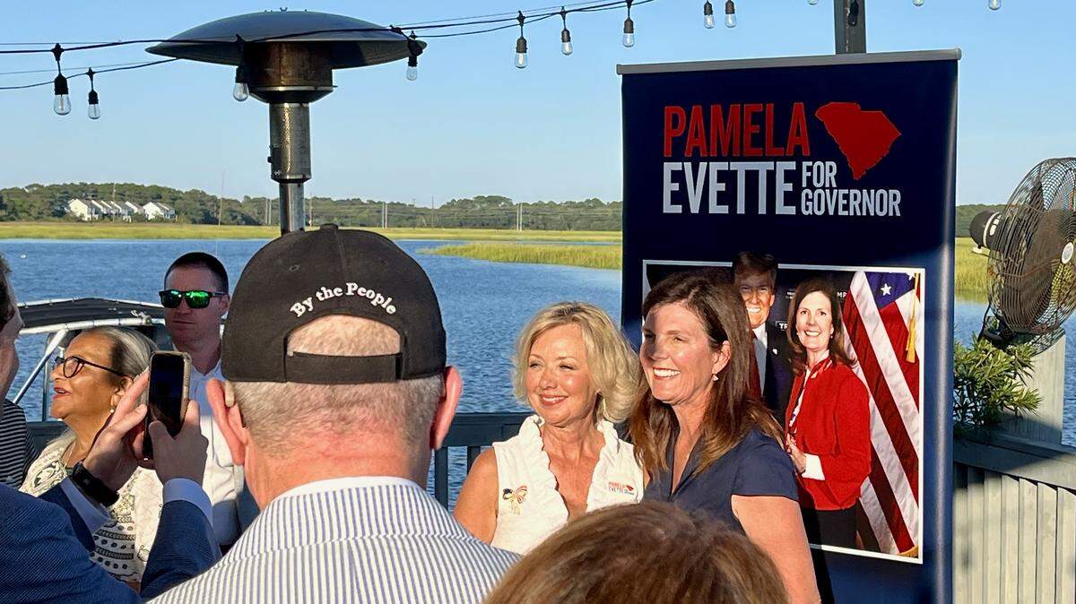 Pamela Evette posing in front of her campaign sign featuring her and Donald Trump with attendees of her town hall at Old Oyster Factory on Hilton Head.