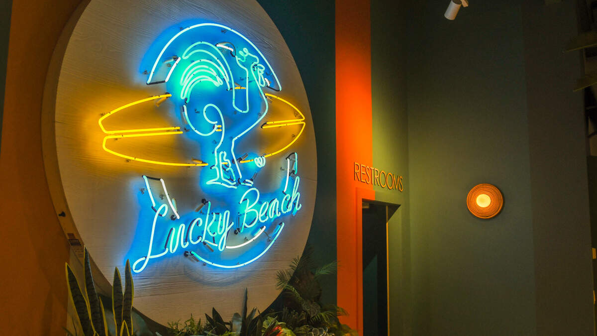 Lucky Beach Bar and Kitchen’s mascot is a rooster carrying a surfboard as seen in neon on the back wall of the restaurant.