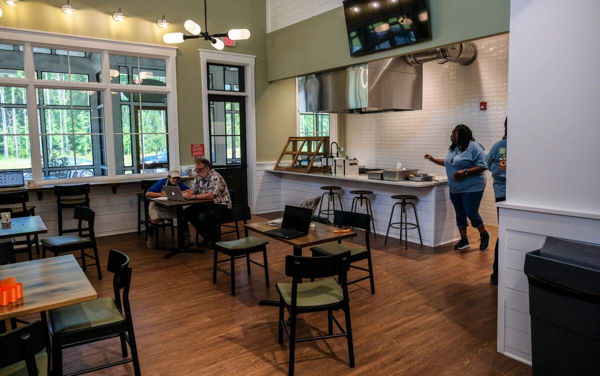 Pictured is the dining area of Lowcountry Fresh Market and Cafe with a door, center, that leads to an outdoor screened porch, as well as an island for cooking and a monitor above to watch as chefs prepare food. In time, the market and cafe will offer cooking classes as well as a supper club, during which patrons can come in after the store closes to have a chosen menu prepared for them.