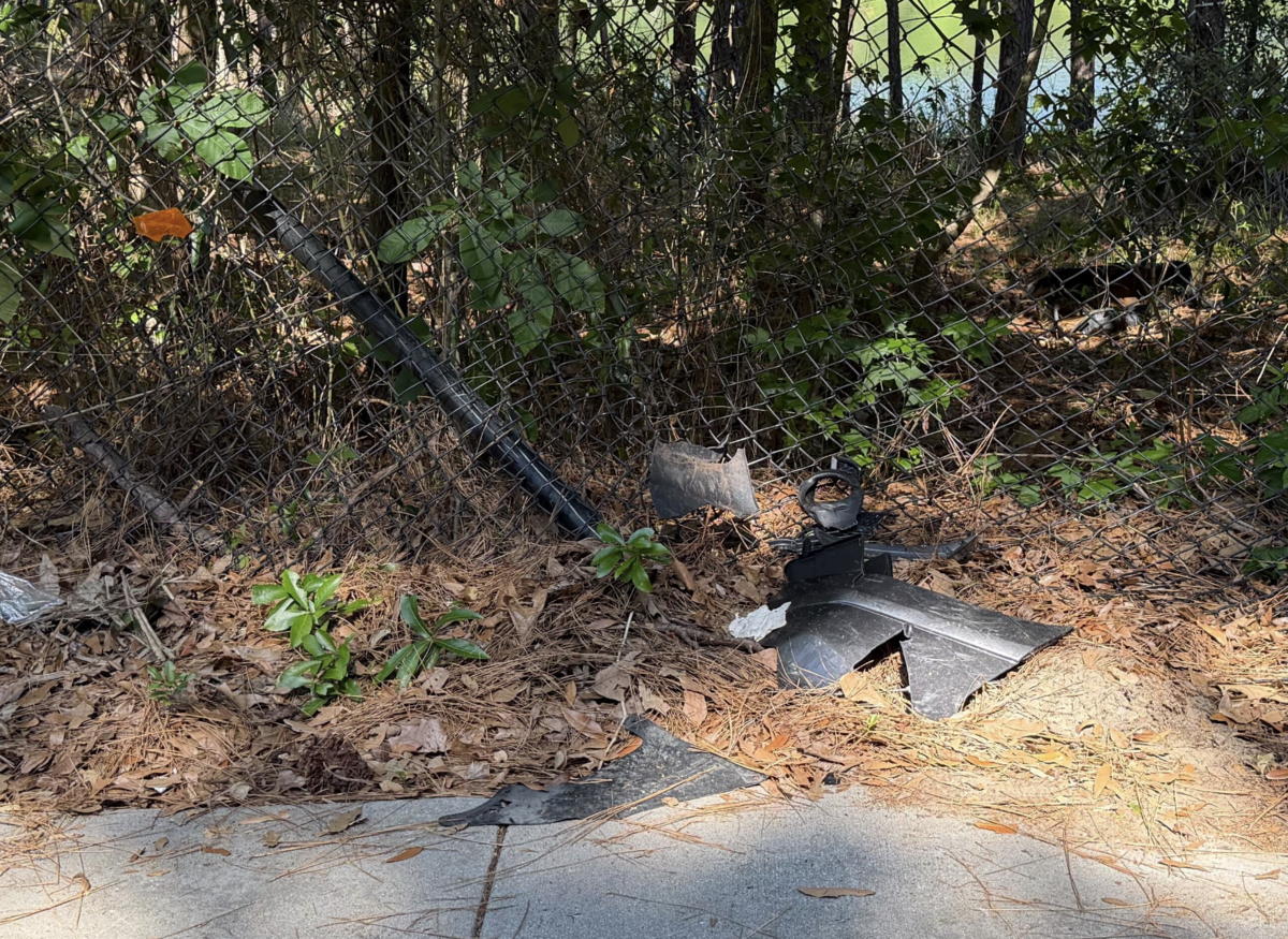 An assortment of car crash debris was photographed beside the road leading to River Ridge Academy on May 19, 2026, nearly two weeks after an alleged drunk driver drove onto the adjoining sidewalk and damaged the fence. Hanging from the caved-in fence was a shattered piece of a car’s reflector.