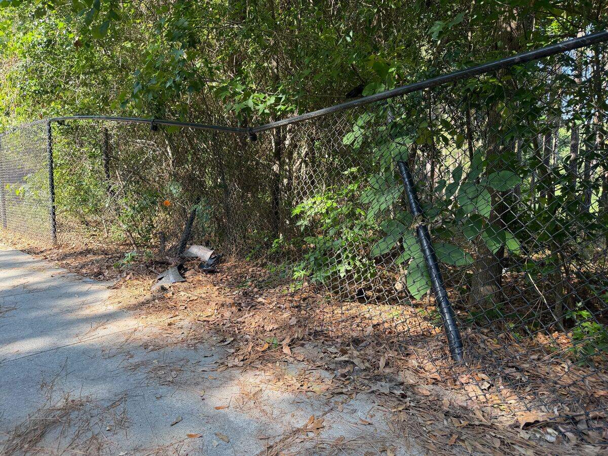 This fence along River Ridge Drive was caved in after being struck by an alleged drunk driver the night of May 6, 2026. A pile of broken car parts was seen near the collision site, and a piece of a car’s reflector hung from the damaged fence nearly two weeks after the crash.