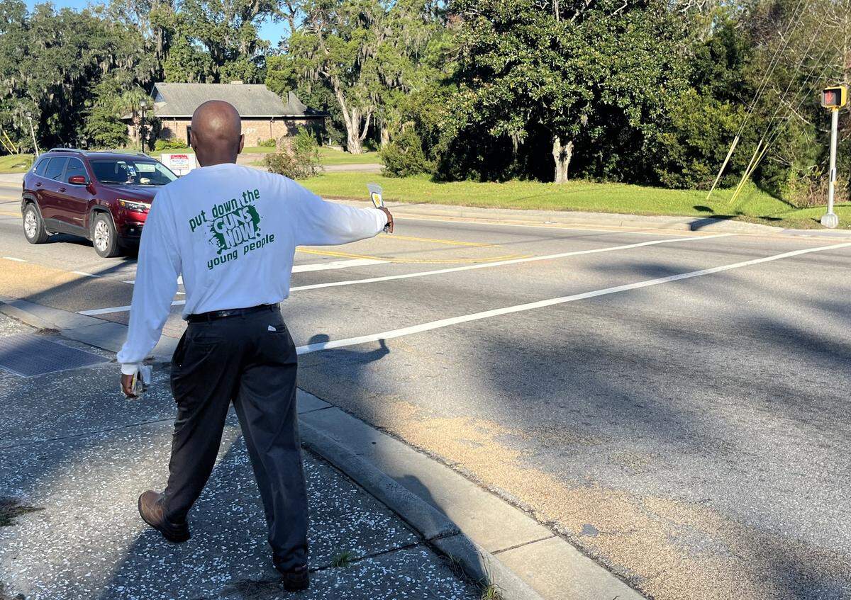 Jack Logan with the nonprofit Put Down the Guns Now Young People passes out information at the corner of Sea Island Parkway and Martin Luther King Jr. Drive Tuesday morning, two days after a shooting at the nearby Willie’s Bar left four people dead and 20 injured.