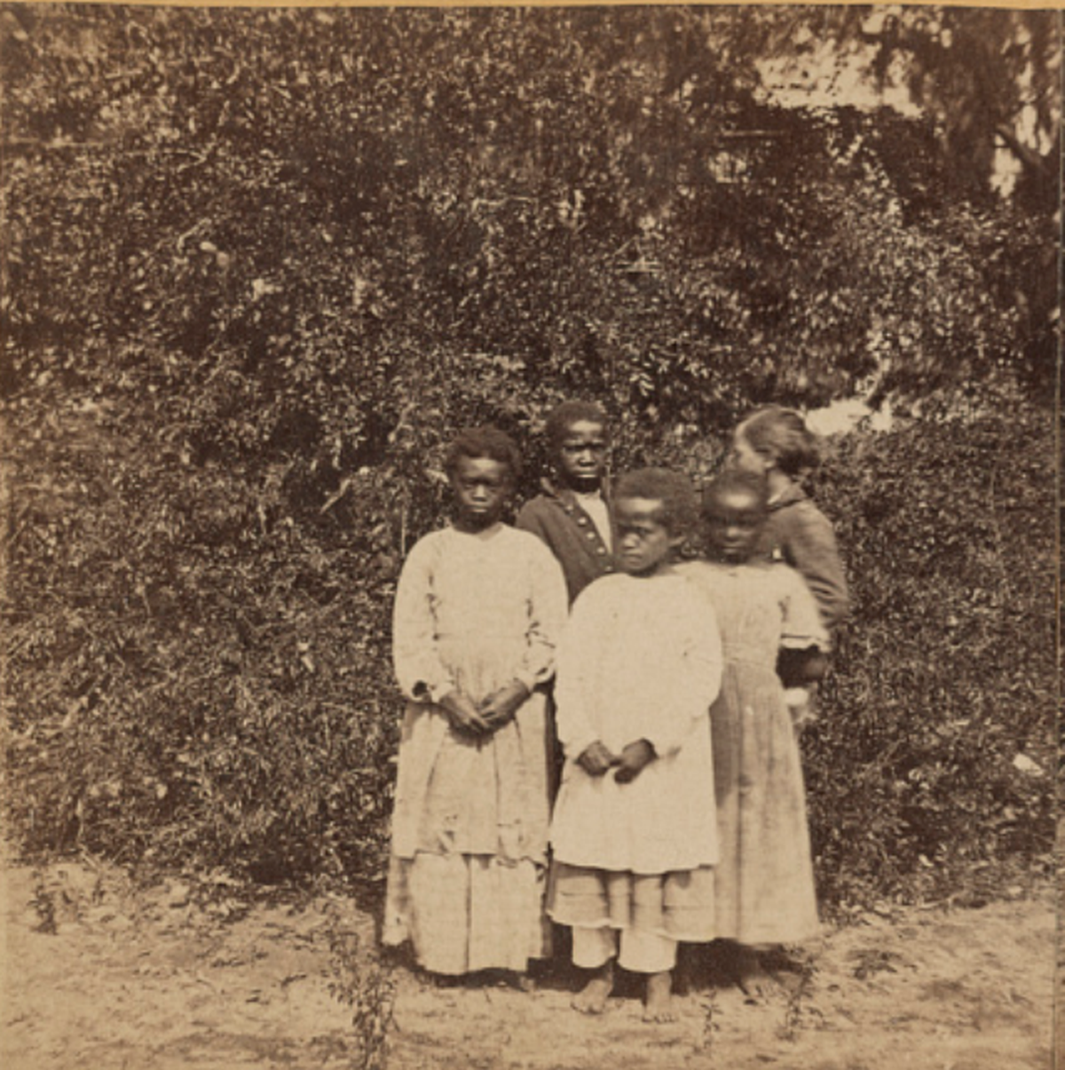 Photograph shows a group portrait of four African American children, the children of Freedmen, and one white child, possibly students at the Penn School in Beaufort, South Carolina.