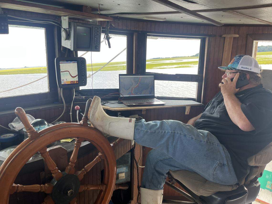 Craig Reaves uses his boot to steer as he talks on the phone as the Gracie Belle moves up Village Creek toward St. Helena Sound where it would spend a few hours trawling for white shrimp.