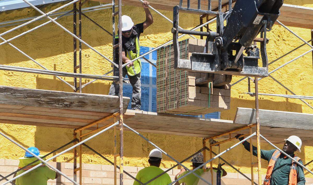 As a supervisor watches, a worker removes a scaffolding bar to allow bricks to be delivered to masons on Wednesday, June 10, 2020 during the expansion construction of River Ridge Academy in Bluffton.