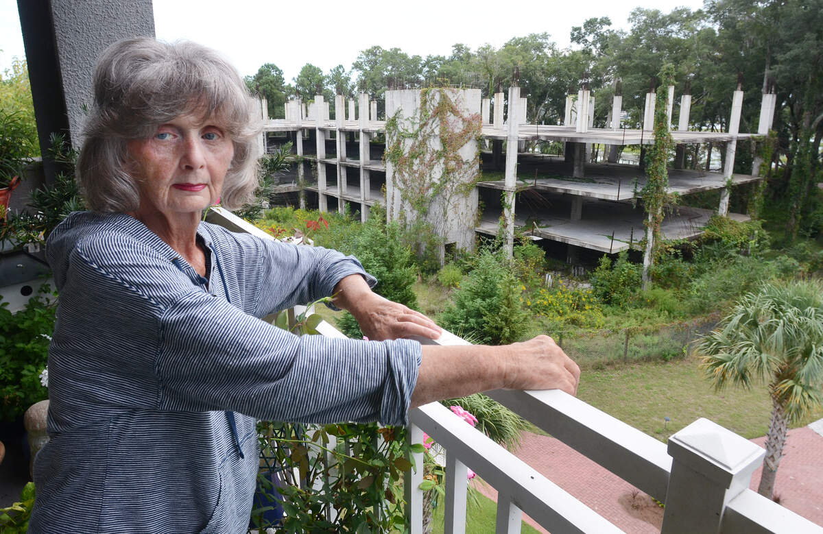 In this photo for a 2014 Packet article, Edgewater resident Jacqueline Heiss stands on her balcony, which overlooks a partially completed building that was abandoned mid-construction several years ago. She said that as long as the building stands incomplete and overgrown, she has little chance of selling her unit for a decent price.