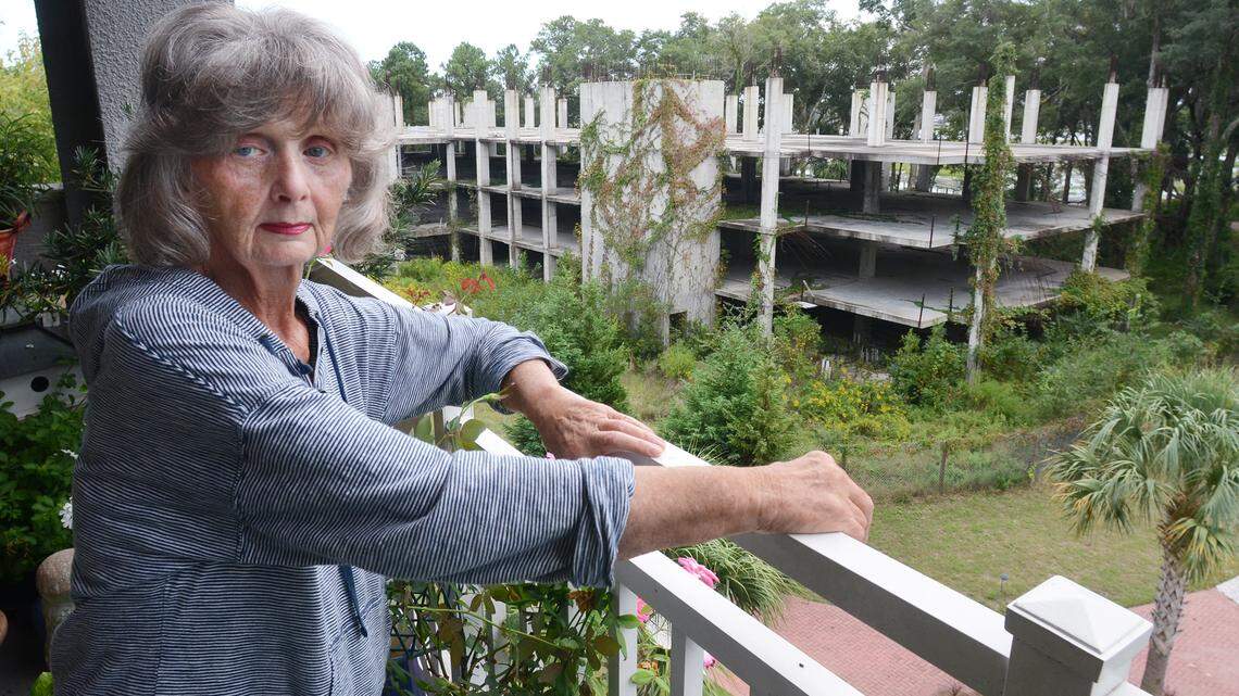 Edgewater resident Jacqueline Heiss stands on her balcony, which overlooks a partially completed building that was abandoned mid-construction several years ago. She says that as long as the building stands incomplete and overgrown, she has little chance of selling her unit for a decent price.
