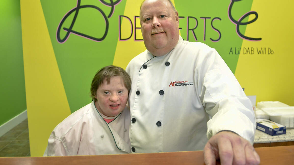 Propietor Russ Gardiner, right, owner of Delectable Desserts by Russ” located along Bluffton Parkway in Bluffton, poses on Thursday morning with his newest employee, Courtney Kawchak. Courtney, who has Down Syndrome, will be a greeter on Sundays at the bakjery. Whle Courtney has liited abilities in retail, Gardiner believes after Courtney becomes accumstomed to her routine, he says, “I think we’ll be able to get her in the back to help decorate cupcakes.”