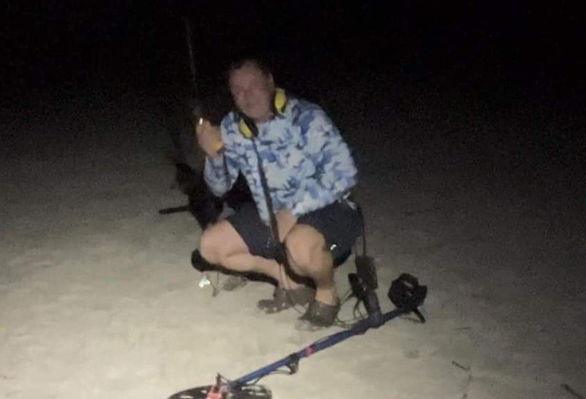 Moye Howard poses with his metal detecting equipment after successfully locating a missing ring during a late-night search on the beach. He uses the Minelab Equinox 800, a state-of-the-art model that costs about $1,000.
