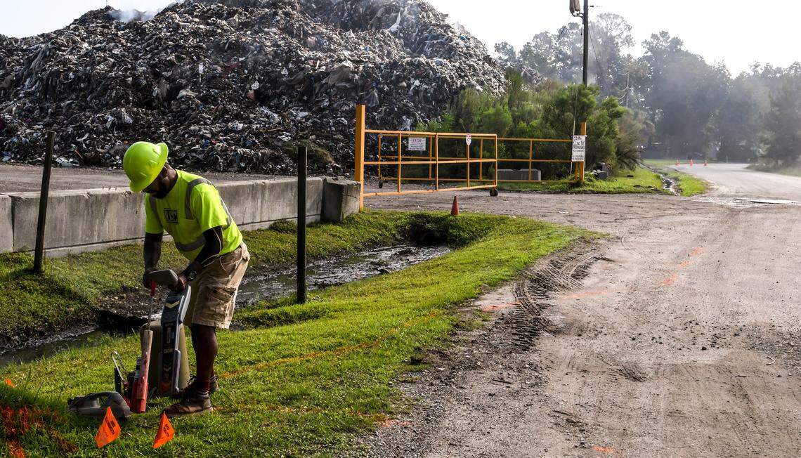 Terrance McLoud with U.S. Infrastructure Company finishes marking underground utilities on Monday morning on Schinger Avenue near the entrance to Able Contracting’s Material Recovery Center just outside Hardeeville town limits. McLoud said the markings will provide guidance if any digging would take place on the unpaved portion of the avenue. Acrid smoke can be seen as it rolls down Schinger Avenue.