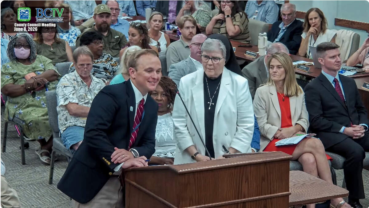 In this screen capture Dylan Kidd, left, interim assistant county administrator, addresses county council as Sister Pamela Smith, right, looks on during the June 8, 2026, Beaufort County Council meeting. Sister Smith was at the meeting to appeal a decision that St. Francis Center on St. Helena Island — a non-profit — must have a business license to operate the charity after requesting a permit for new directional signage on Sea Island Parkway.