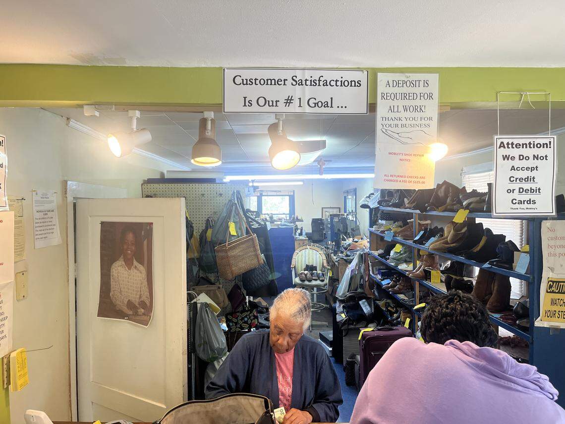 Mary Mobley assists customer Jackie Young of Beaufort at Mobley’s Shoe Repair in Beaufort. A photo of their son, William, who died in 2010, is pinned to the door.