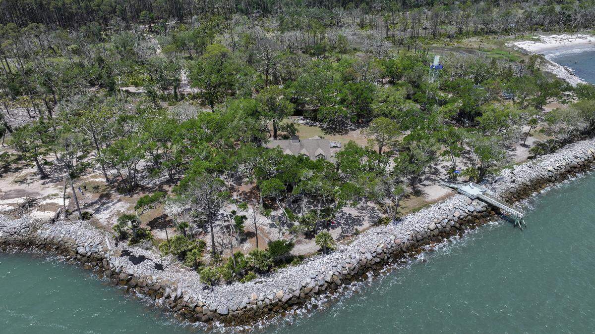 This photo shows the former home of Ted Turner, center, its second-story dormer windows peeking through the live oaks photographed on May 8, 2026, as the Atlantic Ocean laps against the boulders on St. Phillips Island. The caretaker’s home, right, near the water tower, is where Boogie and Jo Tudor would stay when Turner and their guests would come to the barrier island, now owned by South Carolina State Parks.