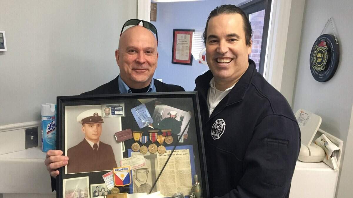 A local pastor Anthony Kollar, the owner of the shadow box, poses for a picture with Burton Fire District Capt. Dan Byrne holding the family memorabilia, both military and fire service, dating back to WWII.