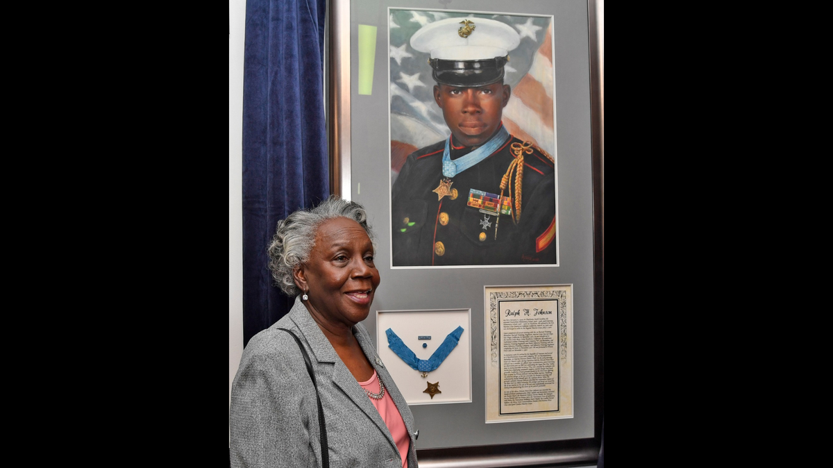 Helen Richards stands with a portrait of her brother and Medal of Honor recipient Ralph Henry Johnson.
